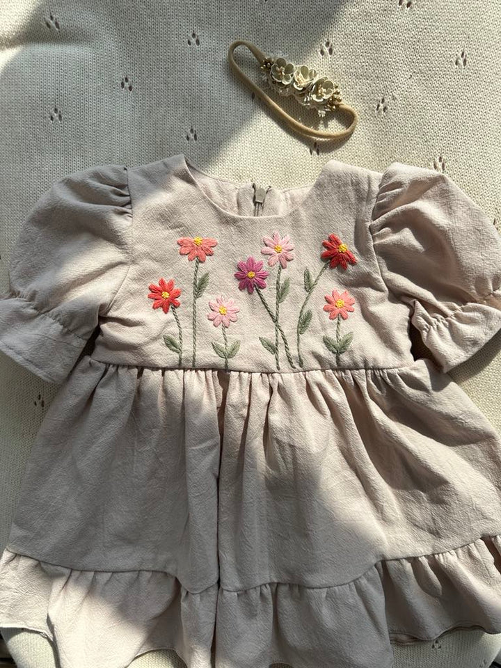 A beige dress with a floral embroidered design on the front, featuring pink and red flowers with green leaves.