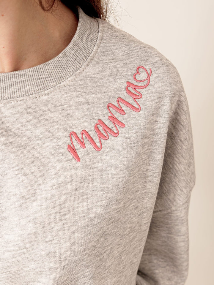 A gray sweatshirt with a pink cursive text embroidered on the front.