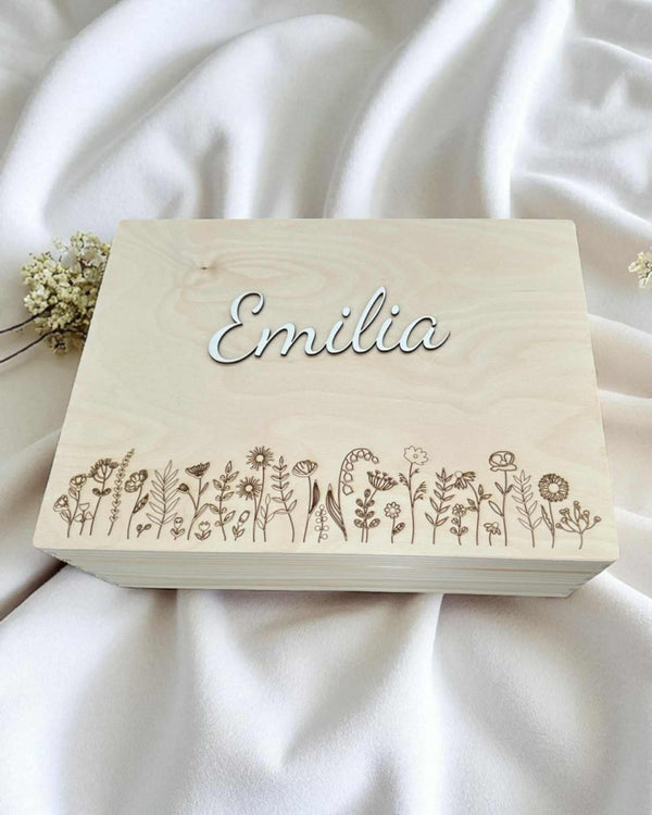 A wooden box with the name "Emilia" engraved on it, surrounded by a row of small floral designs.