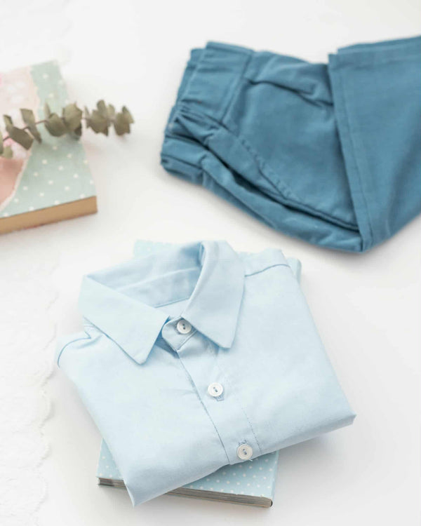 a light blue collared shirt, a pair of blue jeans, and a book with a floral pattern on a white background.