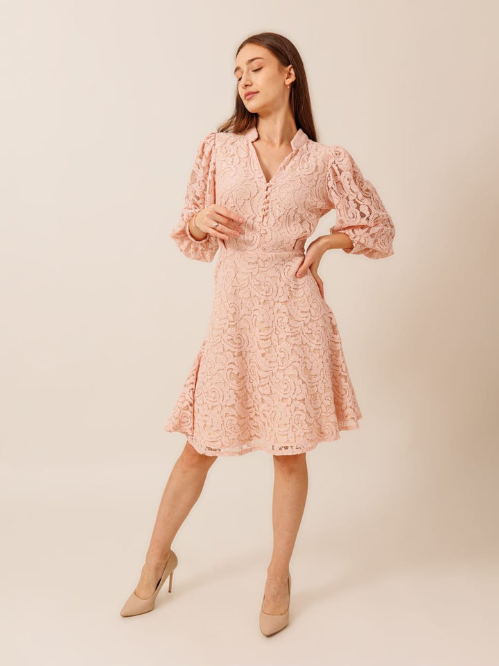 A woman wearing a pink lace dress with puffed sleeves and a short skirt, posing with her hands on her hips.