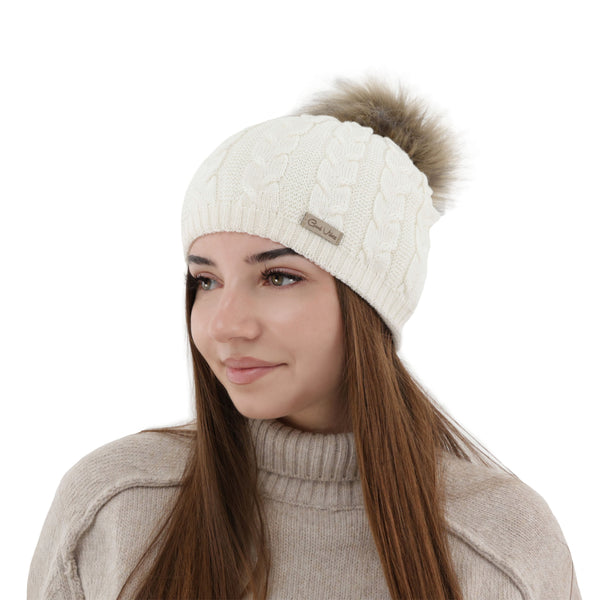 A woman wearing a white knit hat with a fur pom pom, smiling at the camera.