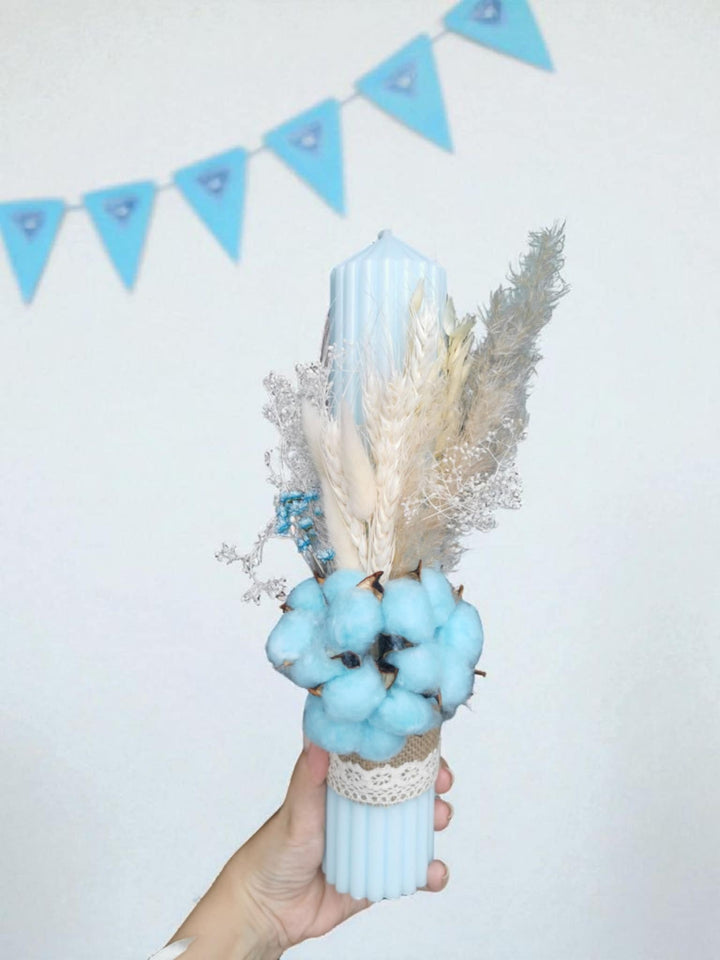 A hand holding a blue candle with dried flowers and cotton balls.