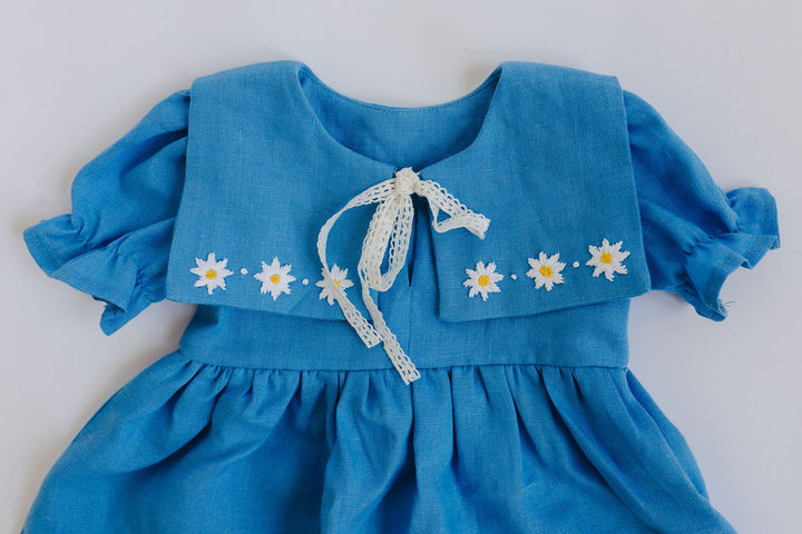 A blue dress with white flowers on the sleeves and a white lace bow at the neckline.