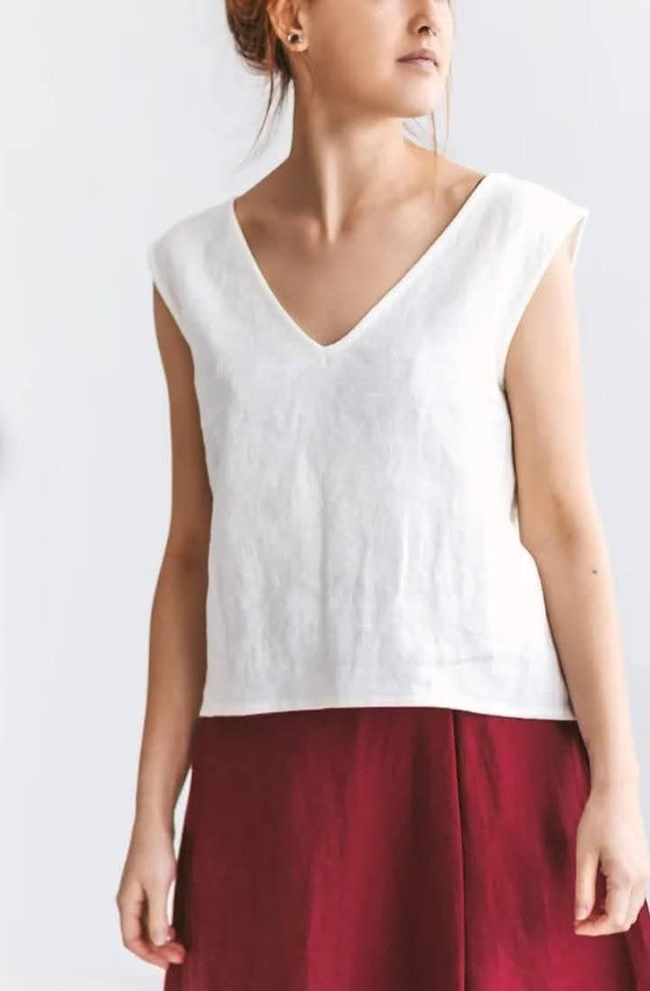 A woman wearing a white sleeveless top and a red skirt stands against a plain background.
