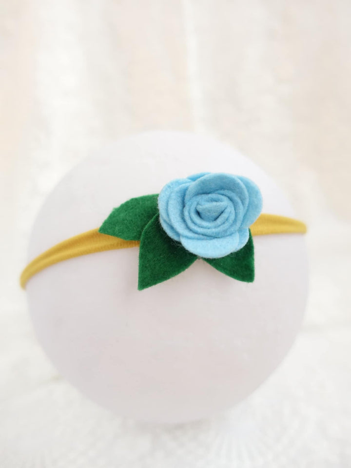 A white round headband with a blue felt rose and green felt leaf attached to it.