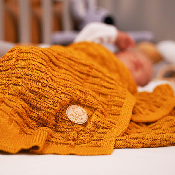 A baby is sleeping peacefully on a bed, wrapped in a cozy yellow blanket.