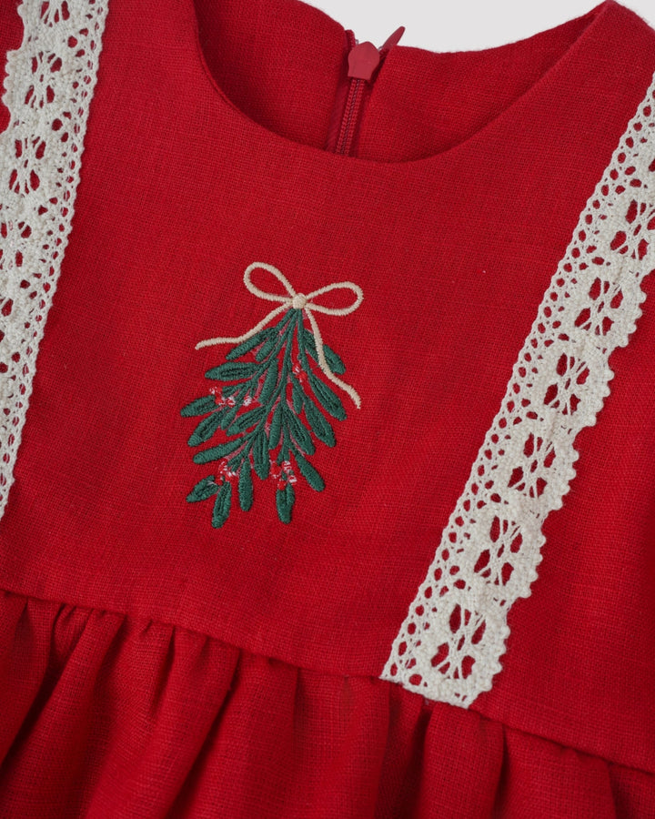 A close-up view of a red dress with a lace trim, featuring a green and red embroidered design on the front.