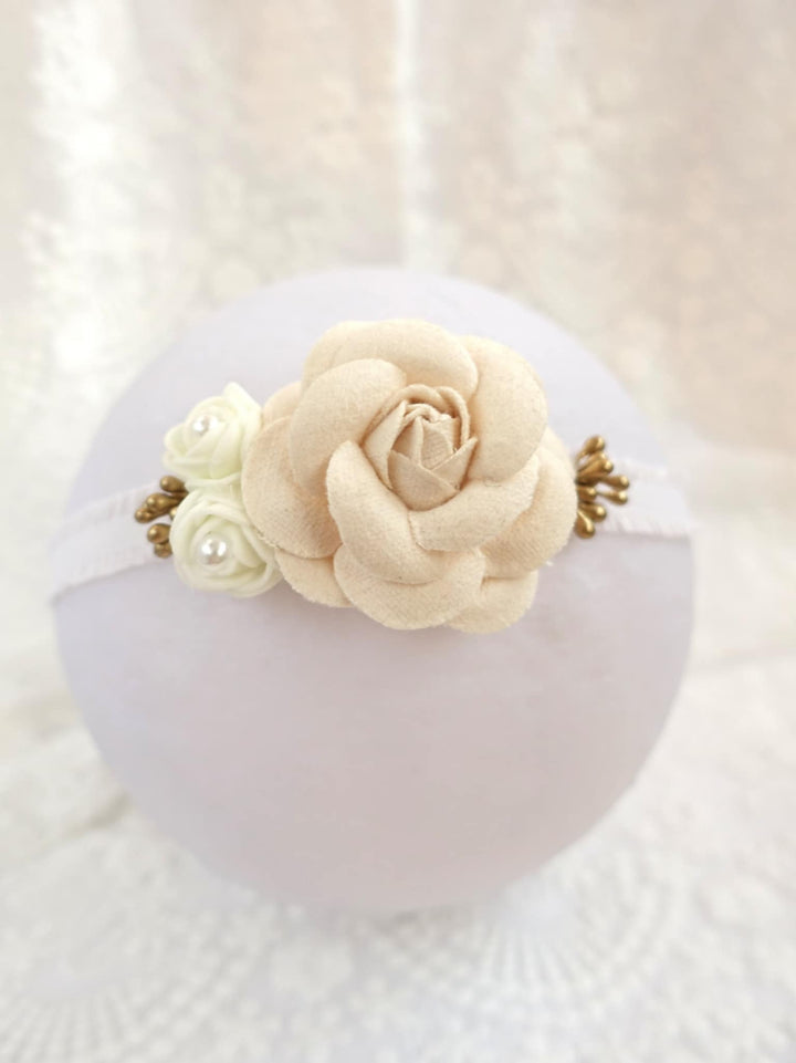 A white headband adorned with a delicate beige rose and white pearls.