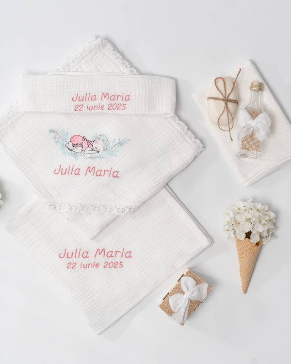 a collection of items, including a white towel with a name embroidered on it, a small gift box, a bottle, and a bouquet of white flowers.