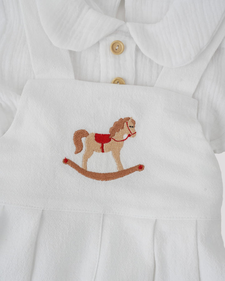 A white dress with a red and brown embroidered image of a rocking horse on the front.