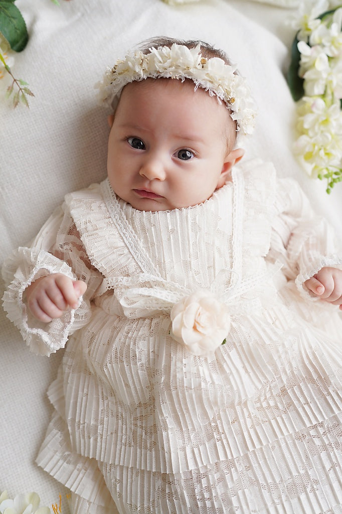 a baby wearing a white dress and a flower headband
