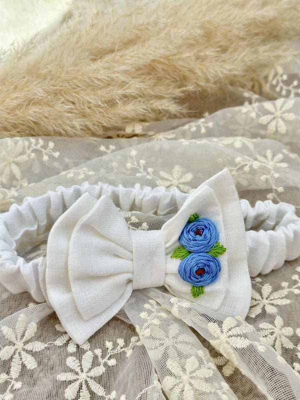 A white bow with blue flowers is placed on a white lace background.