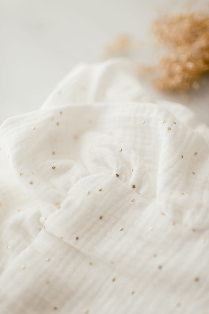a close-up view of a white fabric with small gold dots, creating a textured and shiny appearance.