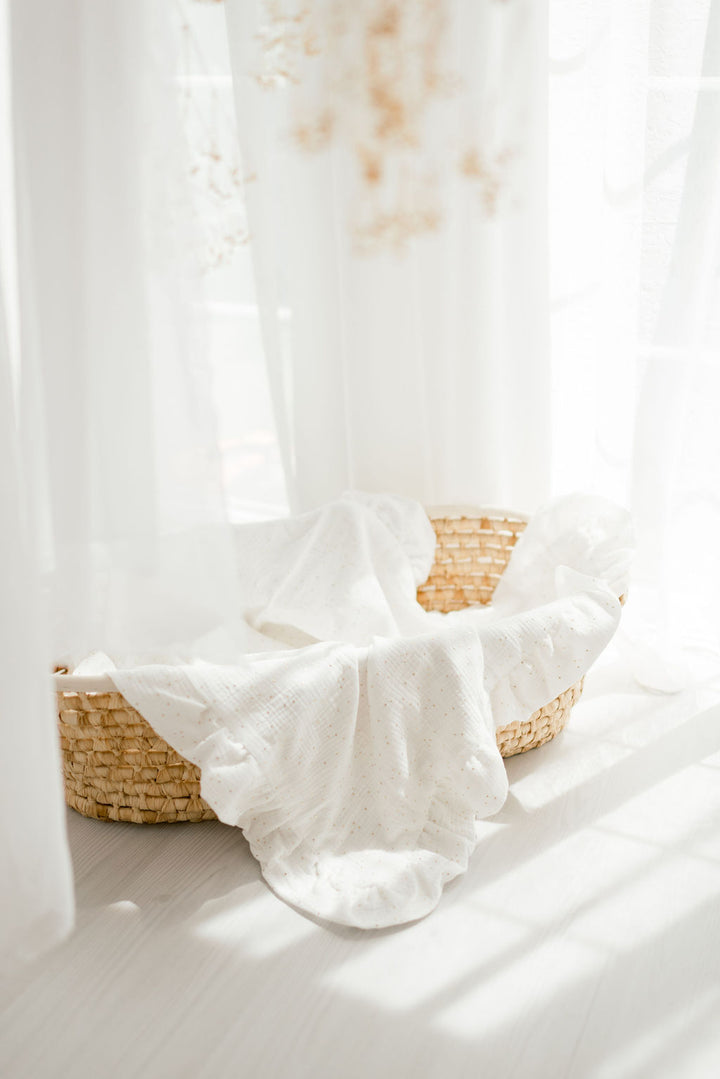 A woven basket filled with white fabric sits on a white surface, with a window and curtains visible in the background.