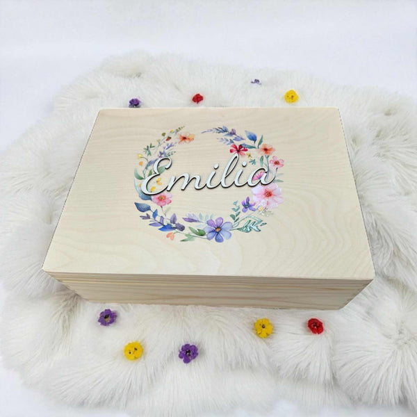 A wooden box with the name "Emilia" written on it, surrounded by a wreath of colorful flowers.