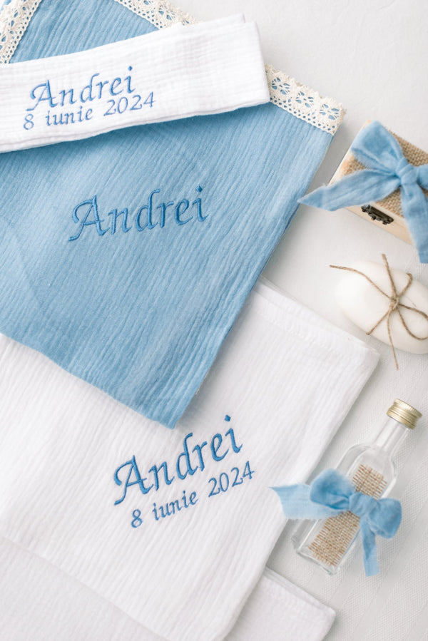 a collection of items, including a blue towel with the name "Andreyi" embroidered on it, a white towel with the same name, and a small bottle with a blue ribbon tied around it. The towels and bottle are arranged on a white surface, creating a visually appealing and organized display.
