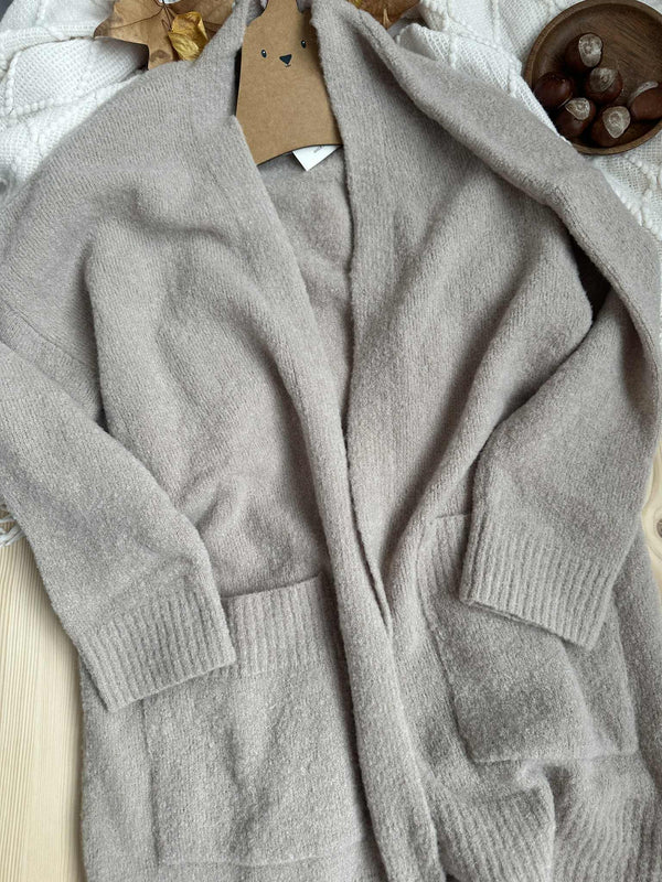 A gray cardigan is draped over a wooden surface, with a small bowl of what appears to be nuts or dried fruit placed nearby.