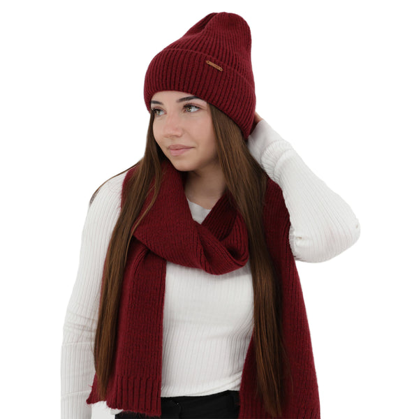 A woman wearing a red knit hat and scarf stands against a white background.