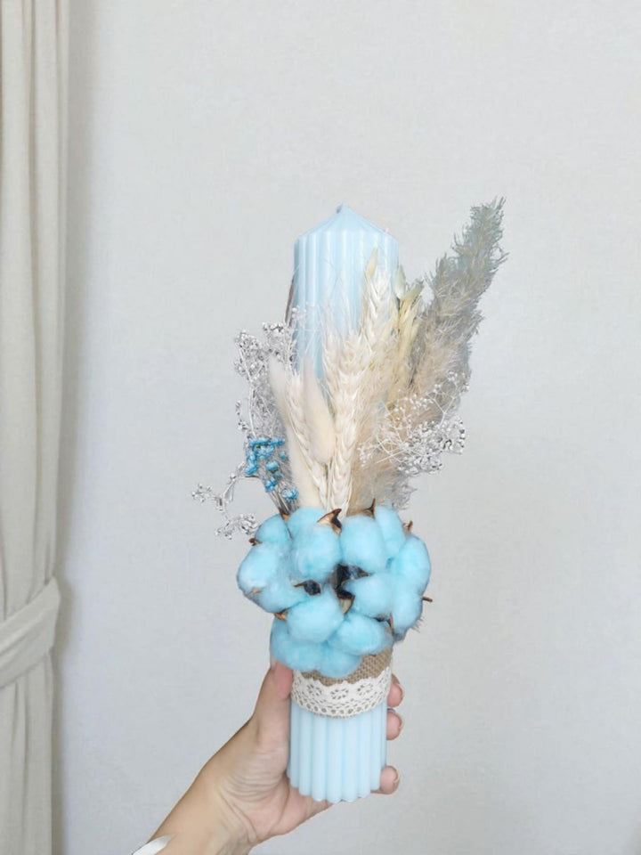 A hand holding a blue candle with dried flowers and cotton balls.