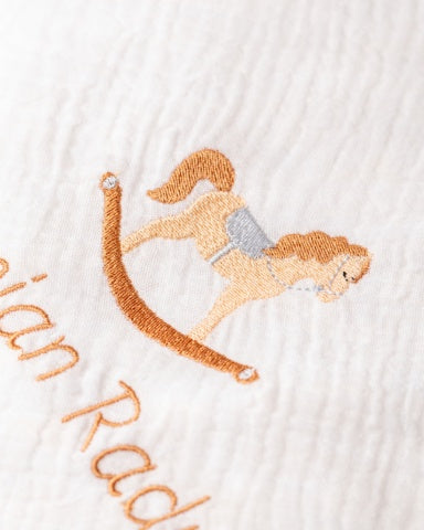 a close-up of a white fabric with an embroidered image of a rocking horse.