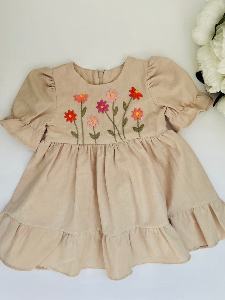 A beige dress with ruffled sleeves and a floral embroidered design on the front.