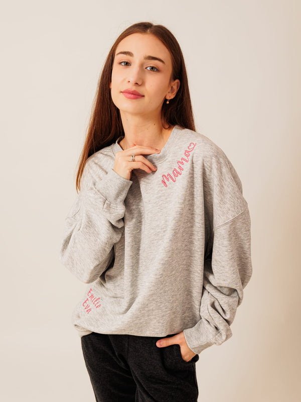 A young woman with long brown hair wearing a gray sweatshirt with the word "Mama" printed on it, posing with her hand on her chin.
