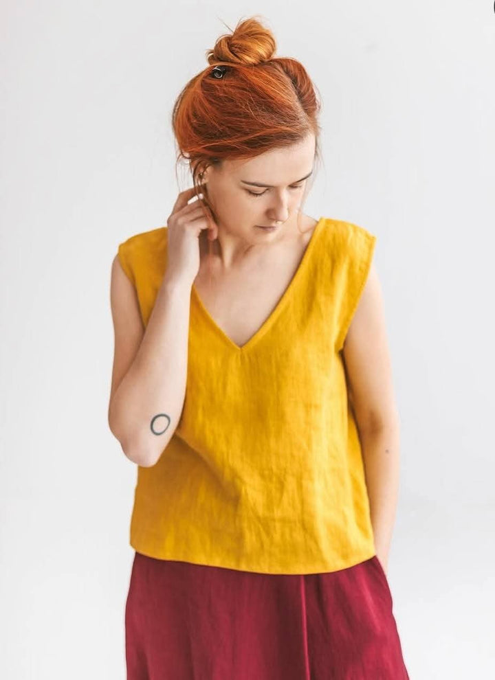 A woman with red hair wearing a yellow sleeveless top and a red skirt is looking down at her hand.