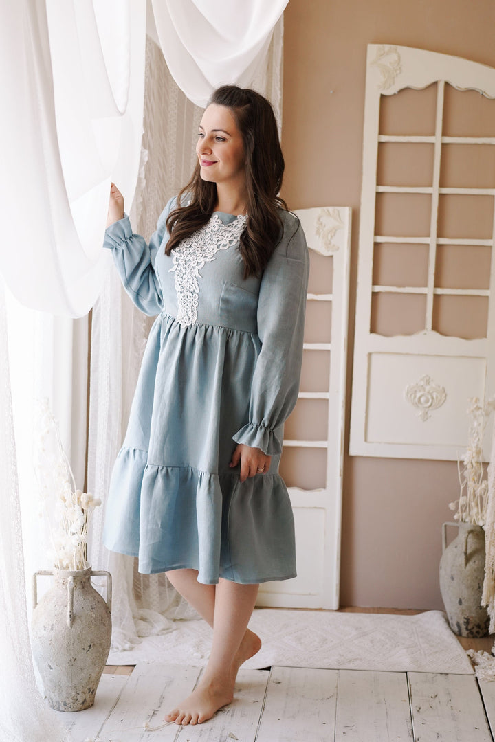 a woman in a blue dress standing in front of a window
