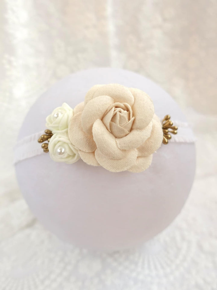A white headband adorned with a delicate rose-shaped flower and pearl accents.