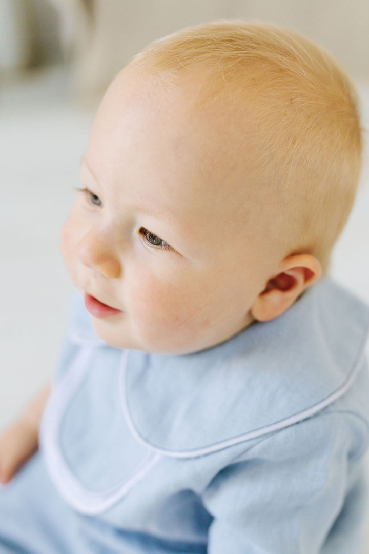 A close-up portrait of a baby with blonde hair, looking to the side with a curious expression.