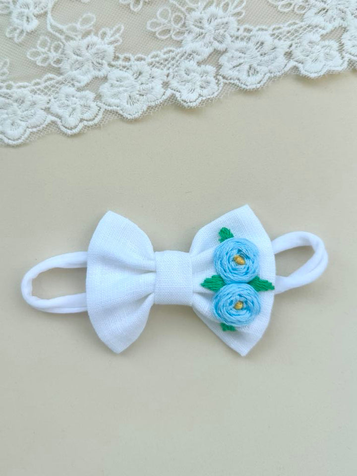 A white bow with blue flowers on it, placed on a white lace background.