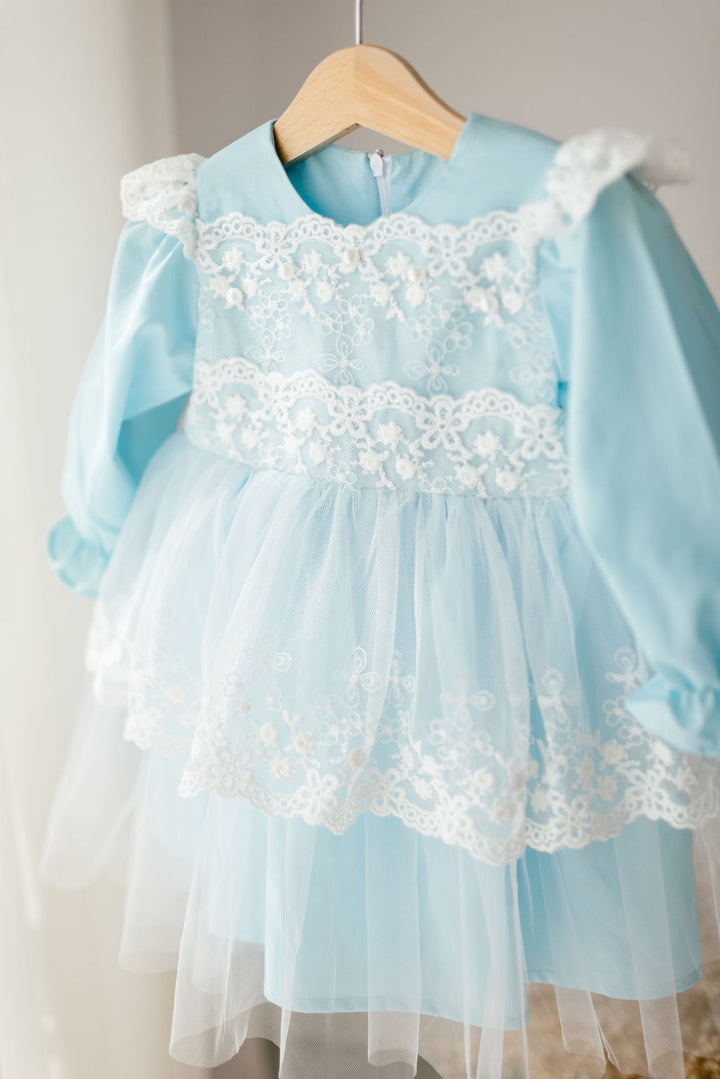 A light blue dress with white lace trim, featuring a ruffled collar and sleeves, is hanging on a wooden hanger.