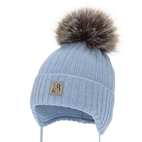 A light blue knit hat with a fluffy fur pom pom on top, featuring a small square patch on the front with the word "ROAR" printed on it.