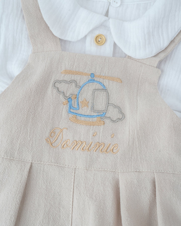 A beige dress with a blue and white embroidered helicopter design and the name "Domnie" written on it.