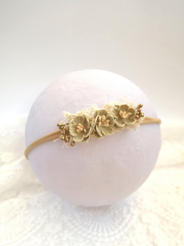 A white headband adorned with delicate gold flowers is displayed against a plain white background.