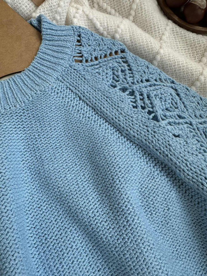 A close-up view of a light blue knitted sweater with a lace-like pattern on the sleeve.