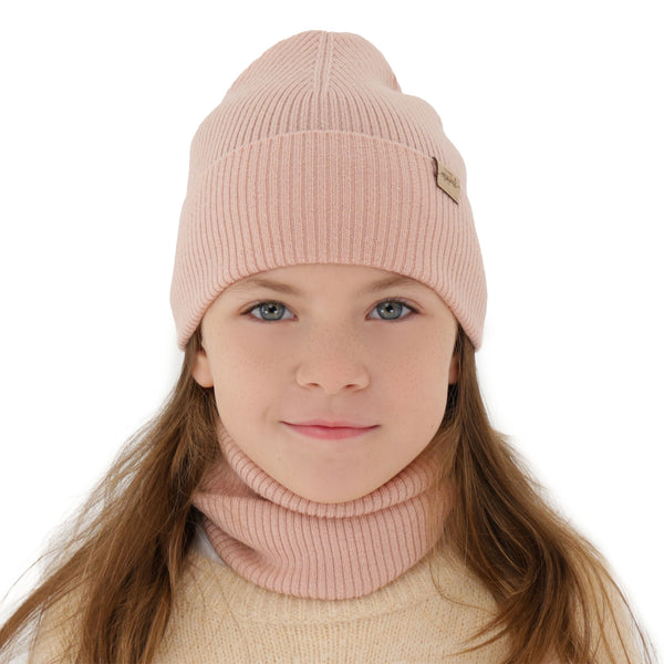 A young girl with long brown hair wearing a pink knit hat and a beige sweater.