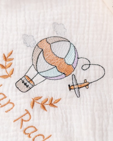 a hand-embroidered hot air balloon, a small airplane, and some leaves, all set against a white background.