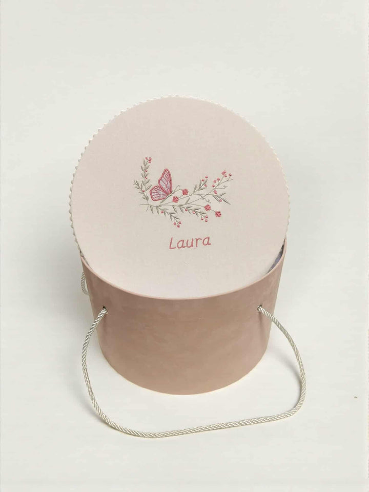 A round, light pink container with a floral design and the name "LaURA" printed on it.