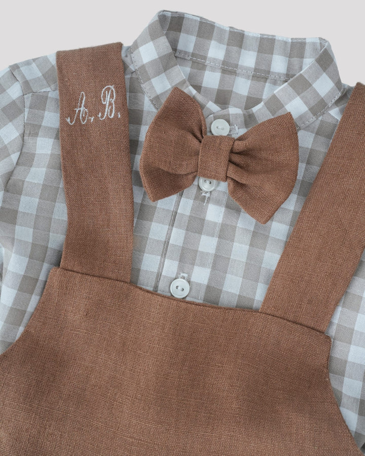 A brown bow tie and a gray and white checkered shirt with a personalized monogrammed initials on the left side of the shirt.