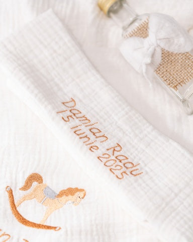 a white towel with a personalized embroidered message, a small glass bottle, and a small rocking horse.