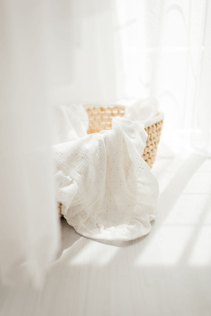 A woven basket filled with white fabric, placed on a white surface, with a window in the background.