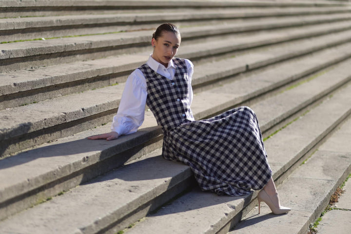 A woman in a checkered dress sits on a set of concrete stairs, looking directly at the camera.