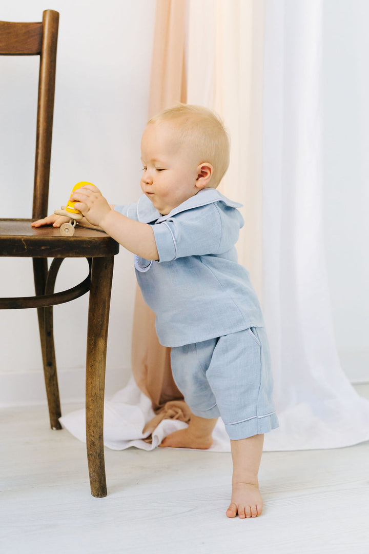 A young child in a blue outfit is standing on a wooden chair, playing with a toy.