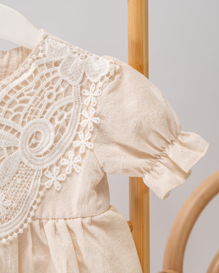A close-up view of a delicate, lace-embellished white dress with a ruffled collar and sleeves, hanging on a wooden hanger.