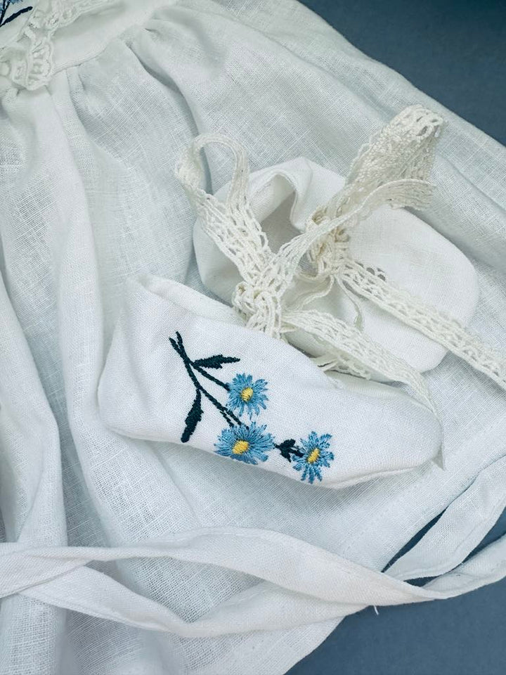 a white dress with blue flowers embroidered on it, along with a white lace item and a white cloth with a lace trim.