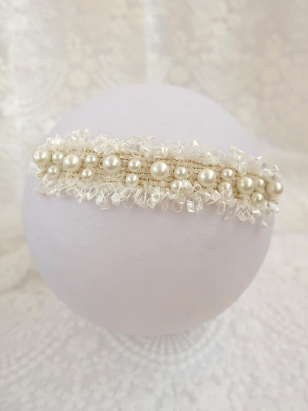 A white, round, white-laced headband adorned with numerous small, round pearls and lace-like embellishments.