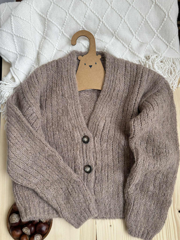 A cozy gray cardigan with buttons and a wooden hanger is displayed on a wooden surface, accompanied by a bowl of nuts.