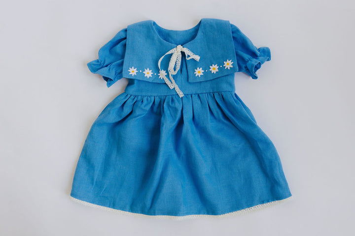 A blue dress with white flowers on the collar and sleeves, laid out on a plain background.